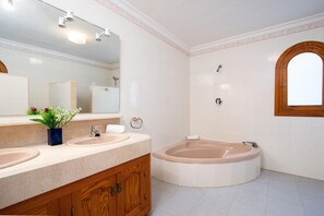 Uma casa de banho com lavatório, duas pias, banheira e um espelho grande.