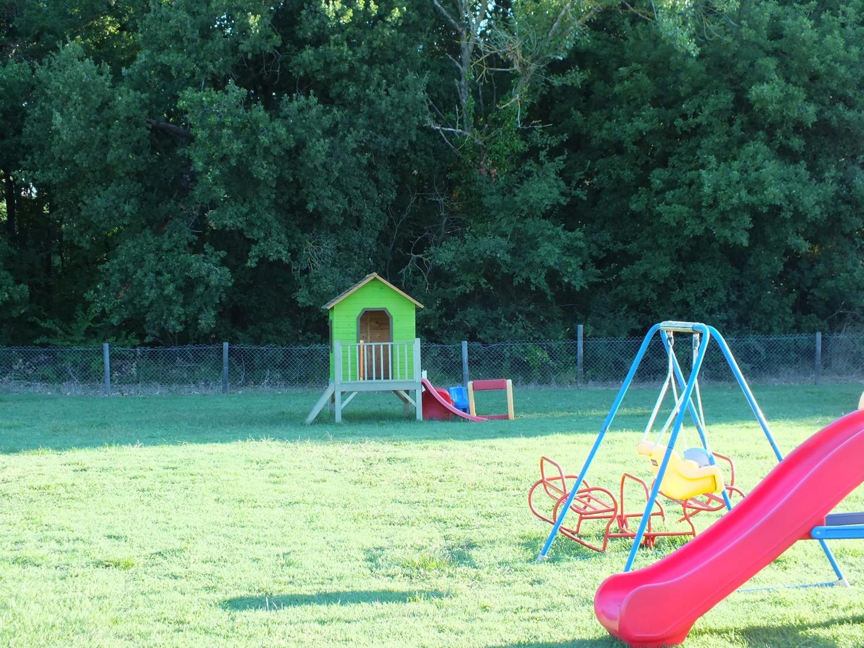 Un'area giochi con uno scivolo, altalene e una piccola casetta verde.