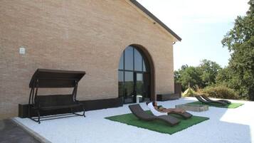 Un edificio con facciata in mattoni, un'ampia porta ad arco e una zona patio con poltrone relax e un'amaca.