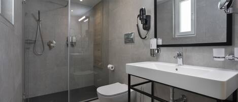 A modern bathroom with a glass-enclosed shower, a toilet, a white sink with a black frame, and a large mirror.