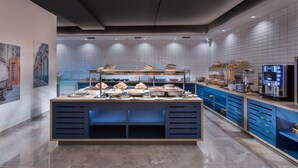 A modern breakfast buffet with a variety of food options, a coffee machine, and a seating area with a view of the cityscape. - Azur Hotel by ST Hotels (Gzira)