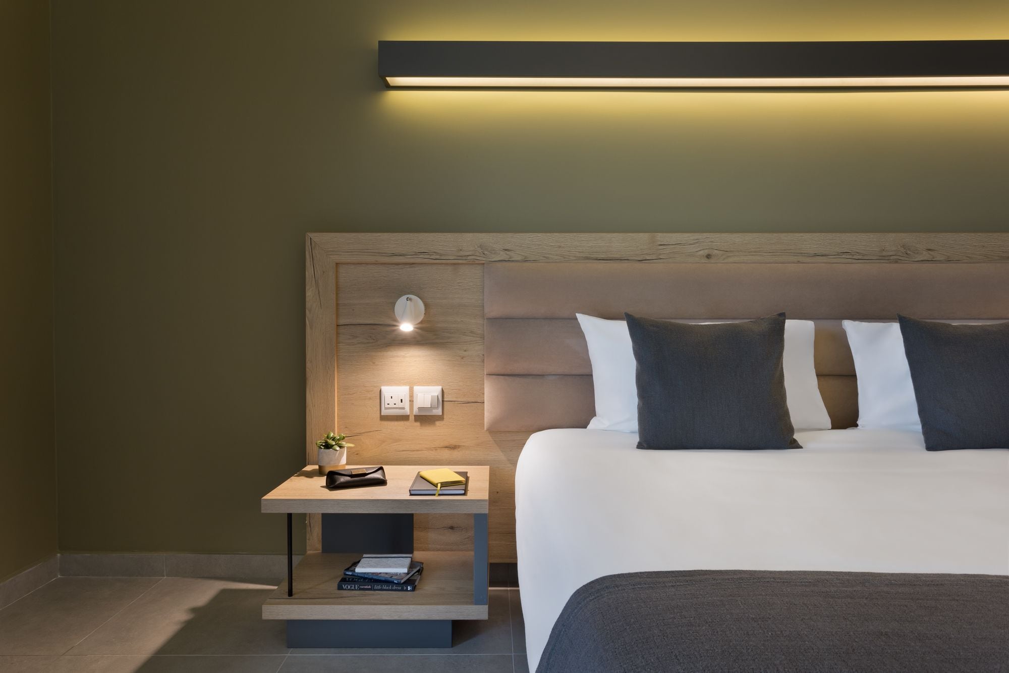 Una habitación de hotel moderna con un cabecero de madera, una mesita de noche con lámpara y una cama bien hecha.