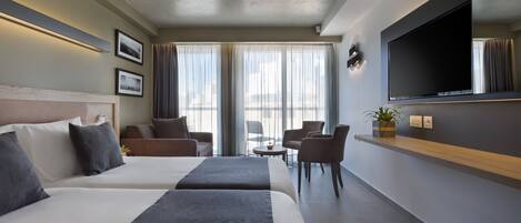 Ein Hotelzimmer mit zwei Betten, einem Fernseher, einem kleinen Tisch und einer Sitzecke mit Sesseln.
