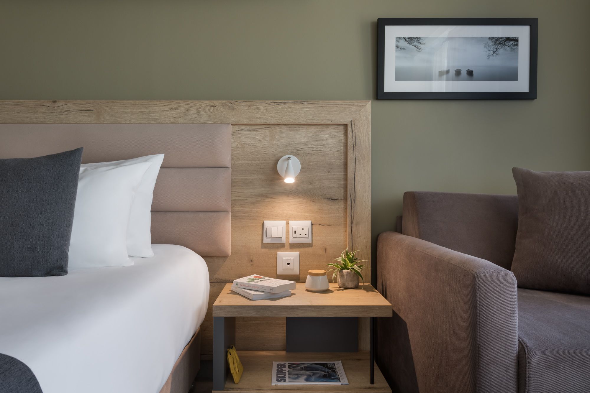 Une chambre d’hôtel avec un lit, une table de chevet avec une lampe, une chaise et un tableau encadré au mur.