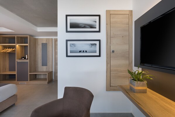 A modern living room with a flat-screen TV, two framed photographs on the wall, a wooden cabinet, and a potted plant. - Azur Hotel by ST Hotels (Gzira)