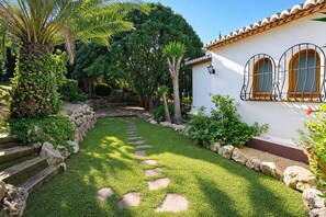 A well-maintained garden with a stone pathway leading to a white building with arched windows. - Laurel 8 pax - Javea, Costa Blanca (Javea)