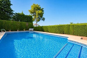 A clear blue swimming pool with a bench and potted plants, surrounded by neatly trimmed hedges.