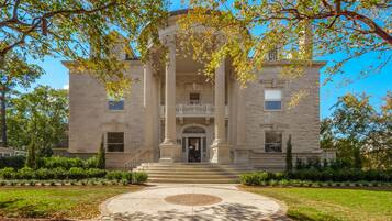 Stately building with a classical facade, surrounded by a manicured lawn and a circular pathway.
