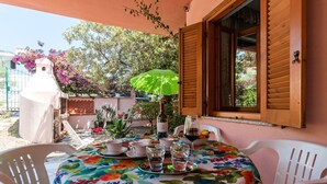 An outdoor patio with a table set for two, surrounded by white plastic chairs, a green umbrella, and a bottle of wine. - Calagonone Villa with garden bbq, WiFi / AC --- IUN Code: P2169 (Dorgali)