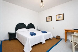 Une chambre à coucher avec un lit double, deux tables de chevet, une petite table, une chaise et deux tableaux encadrés au mur.