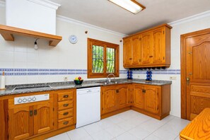 A kitchen with wooden cabinets, a dishwasher, a sink, and a window with a view of greenery.