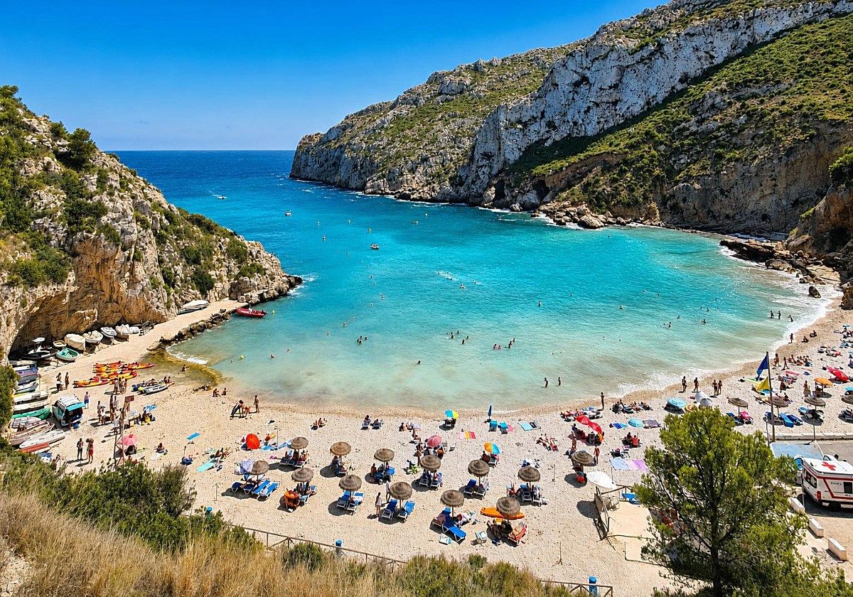 A beach with clear turquoise water, rocky cliffs, and a variety of beach umbrellas and sun loungers.