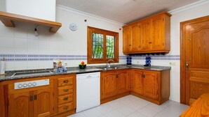 Een keuken met houten kastjes, een inbouwvaatwasser, een granieten aanrechtblad en een raam met uitzicht op groen.