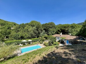 A house with a swimming pool surrounded by lush greenery and hills in the background.
