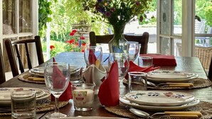 Een eettafel gedekt voor vier personen, met een bloevas, wijnglazen en borden.