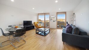 A modern living room with a dining area, a sofa, a coffee table, and a TV. - 1 Bedroom Stylish Apartment near Regents Park FREE WIFI & AIRCON by City Stay Aparts London (London)