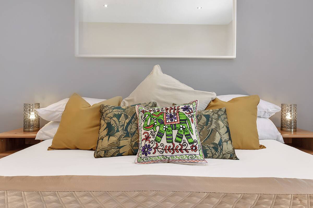 A neatly made bed with patterned pillows and a decorative wall hanging above.