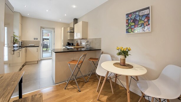 A modern kitchen with a dining area, including a table with chairs, a small island, and a painting on the wall. - Finding My Palace in Tooting (London)