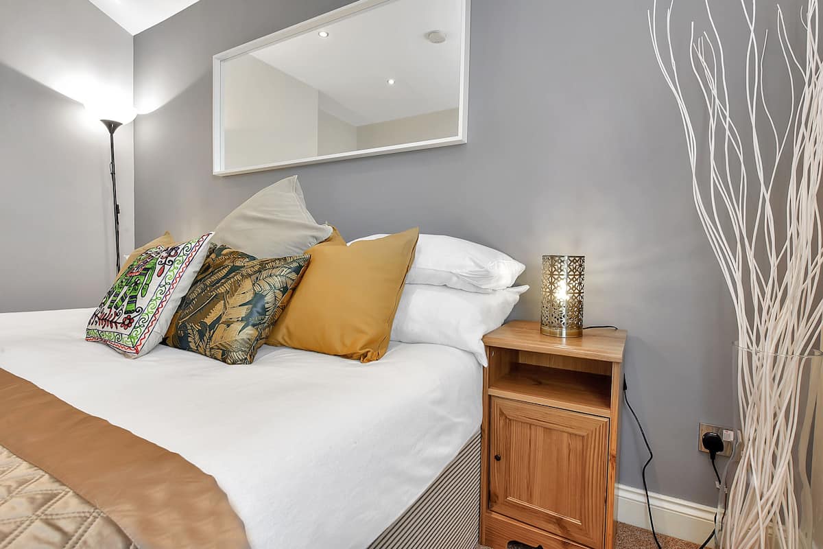 A bedroom with a bed, bedside table, lamp, and a mirror.
