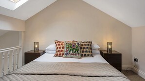 A bedroom with a sloped ceiling, a skylight, a bed with patterned pillows, two bedside lamps, and a power outlet on the wall. - Finding My Palace in Tooting (London)