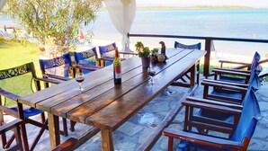An outdoor dining area with a wooden table and chairs, a bottle of wine, and a potted plant. - Anna Karra Studios & Apartments (Sithonia)