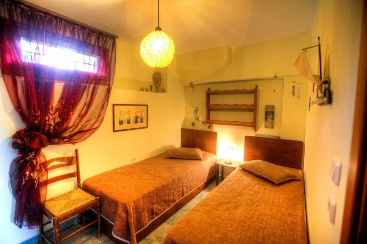 Ein Zimmer mit zwei Einzelbetten, einem Holzstuhl, einem Tisch und einer Pendelleuchte.