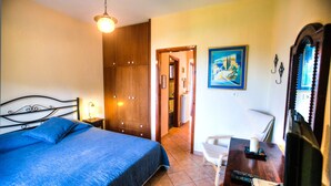 A bedroom with a bed, a desk with a chair, a desk lamp, a painting, and a mirror. - Anna Karra Studios & Apartments (Sithonia)