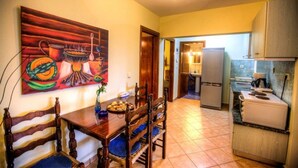 A kitchen with wooden chairs, a dining table, and a painting on the wall. - Anna Karra Studios & Apartments (Sithonia)