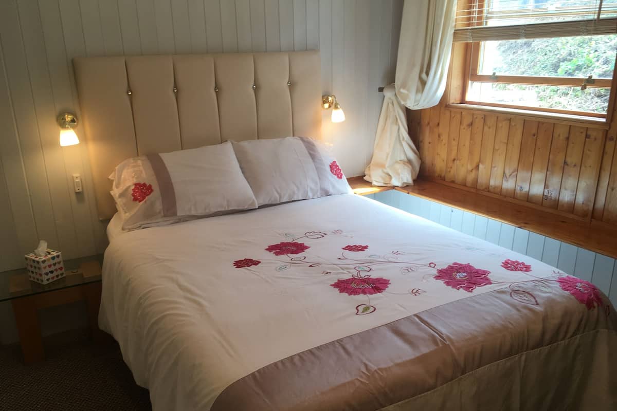 A neatly made bed with a floral bedspread, a headboard with light-colored panels, and a window with curtains.