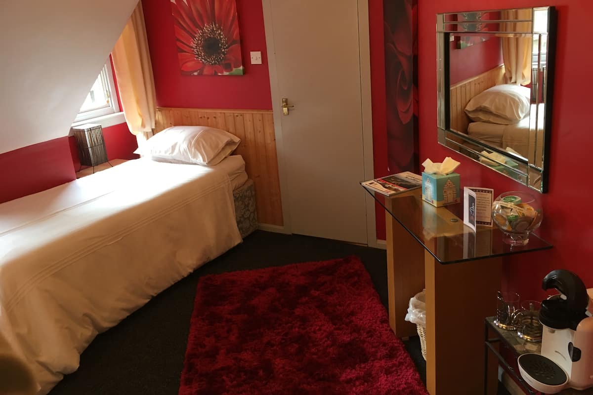 A bedroom with a bed, a desk with a mirror, a red rug, and a window with curtains.