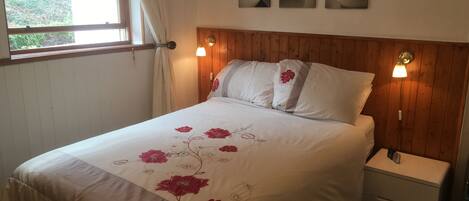 A neatly made bed with floral bedding, a wooden headboard, a bedside lamp, and a nightstand with a phone.