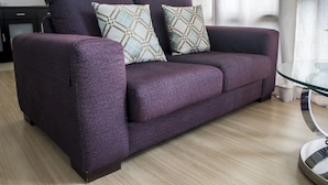 Un canapé violet agrémenté de coussins à motifs, dans un salon moderne doté d’une table basse en verre.