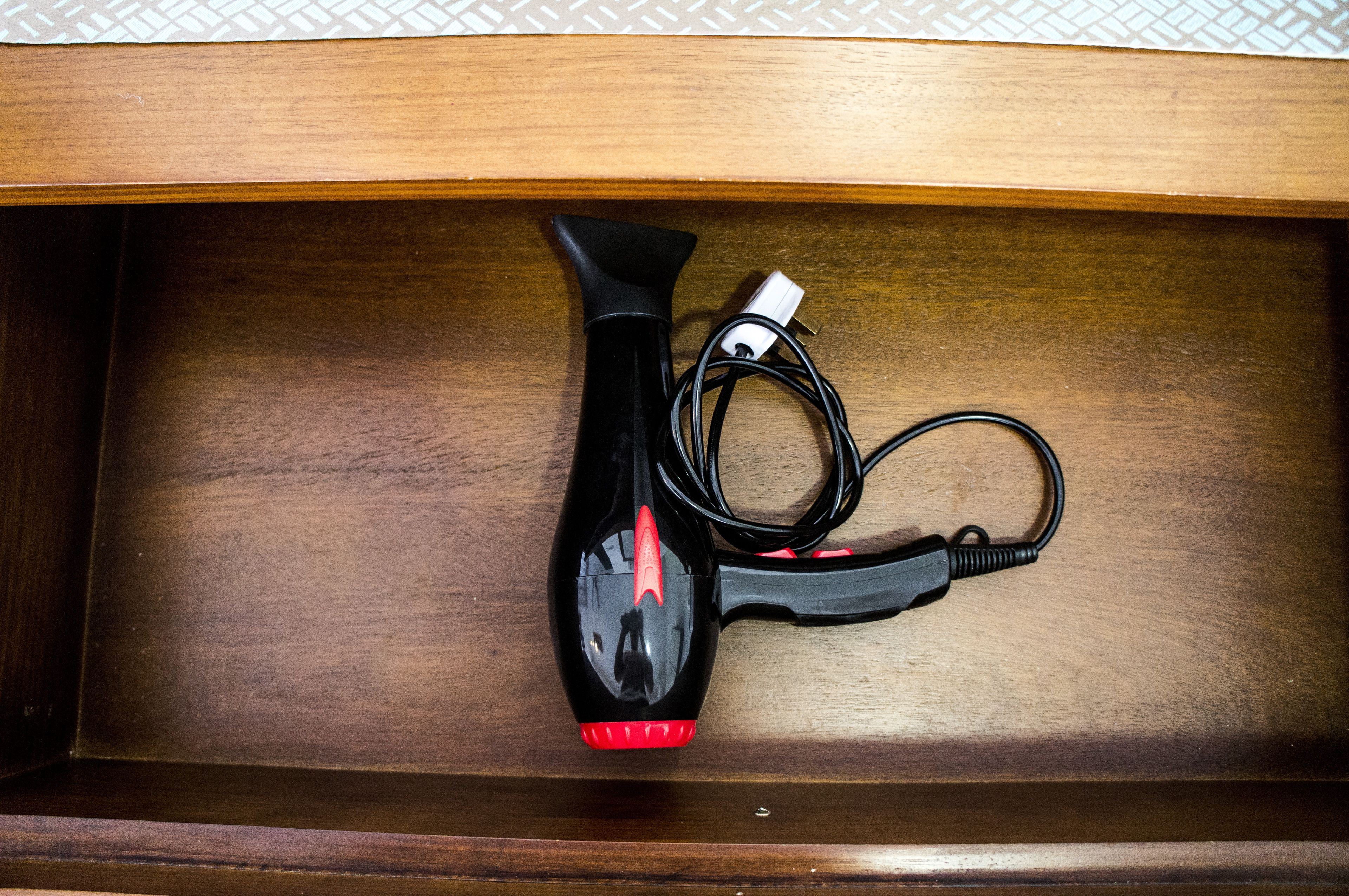 A wooden drawer with a black hairdryer and its power cord inside.
