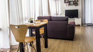 Un salon moderne avec une table à manger en bois, un canapé violet et un téléviseur posé sur un meuble blanc.