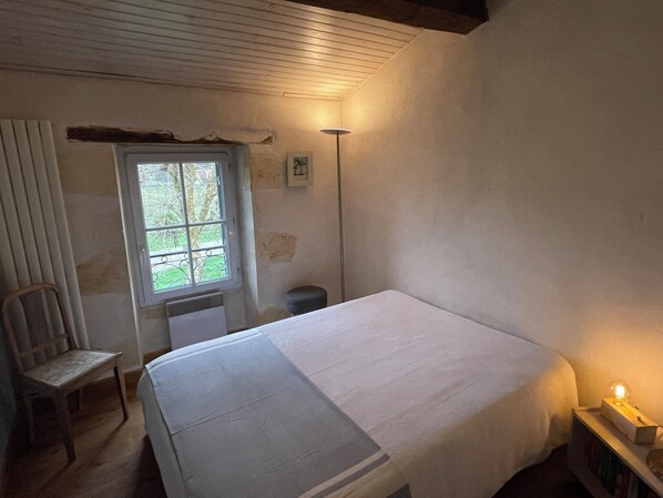 Une chambre à coucher avec un lit, une chaise, une fenêtre et une table de chevet avec une lampe.