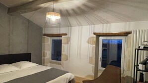 Un dormitorio con cama, una silla, lámpara colgante, ventana y puerta.