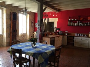Una cocina con pared roja, mantel azul y blanco a cuadros, y un jarrón con flores.