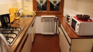 Een compacte keuken met een gasfornuis, een magnetron en een klein spoelbakje.