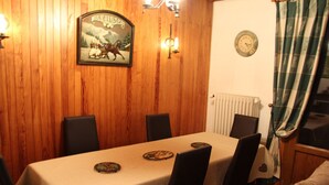 Een eetruimte met een wand bekleed met houtpaneel, een tafel met tafelkleed en stoelen.