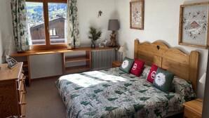 Een slaapkamer met een houten bureau, een bed met een quilt en een raam met gordijnen.