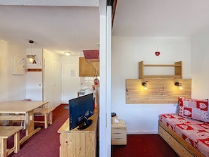 Quarto com escrivaninha de madeira, computador, sofá vermelho e prateleira com iluminação.