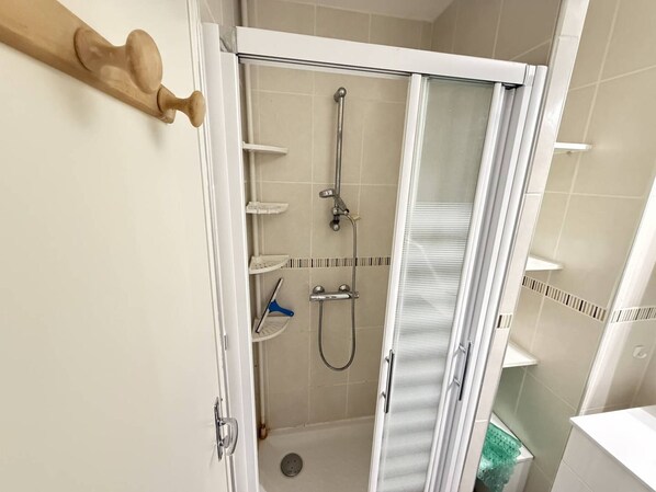 Une douche avec une porte en verre, un sèche-mains et une étagère.