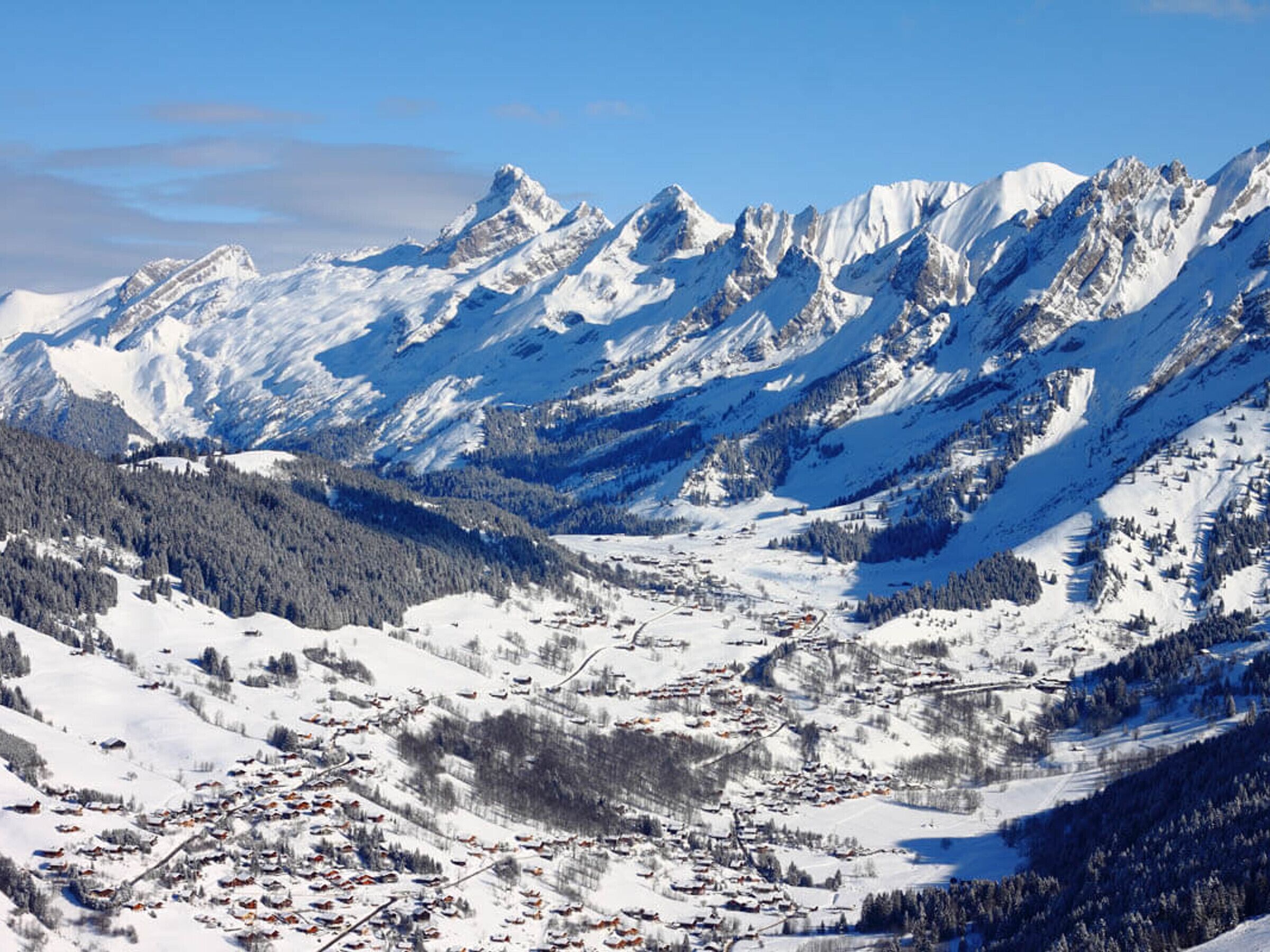 Une chaîne de montagnes enneigées, avec une ville située dans une vallée au premier plan.