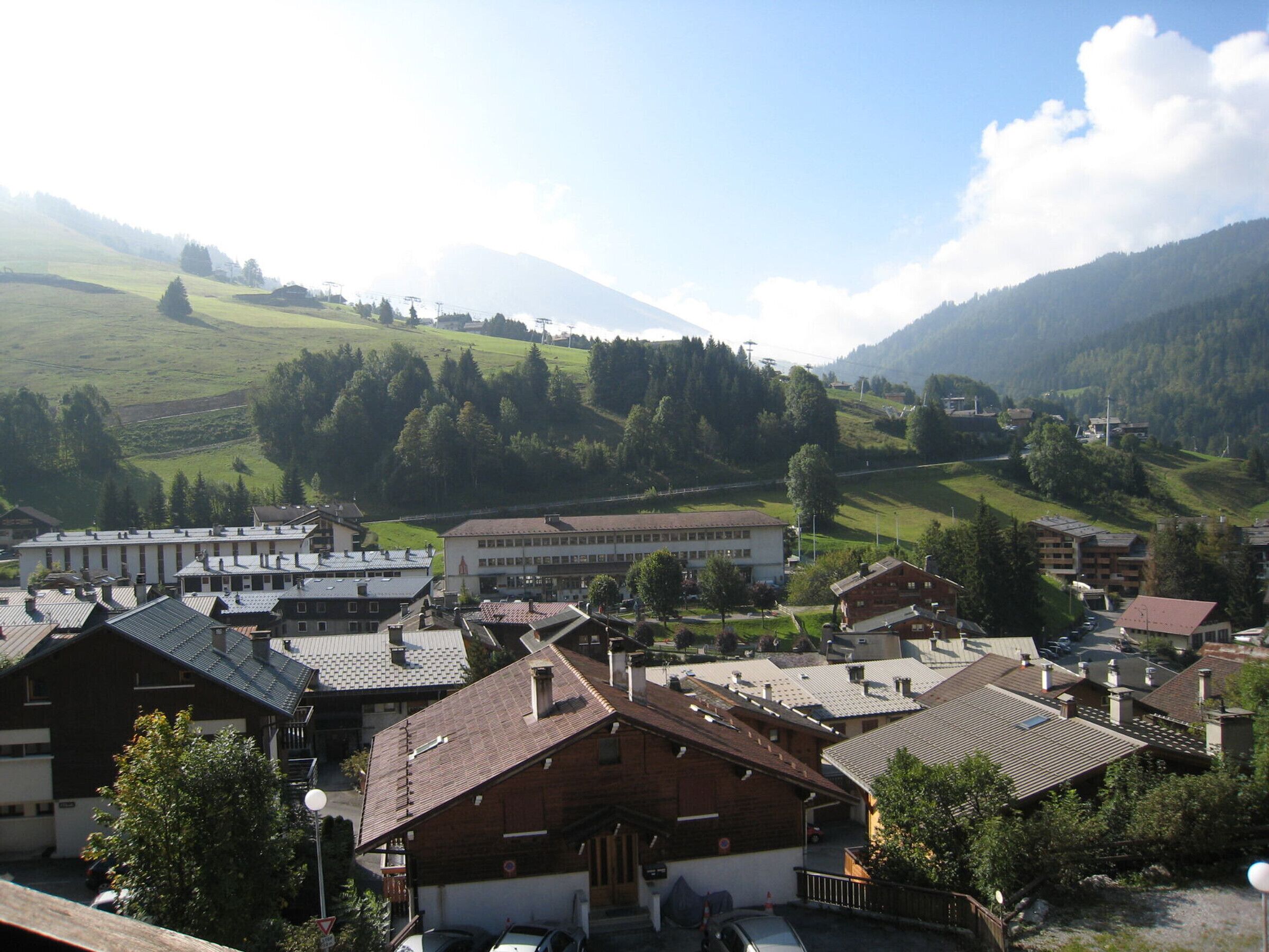 A town with traditional architecture, including a mix of residential and commercial buildings, set against a backdrop of green hills and a mountain.