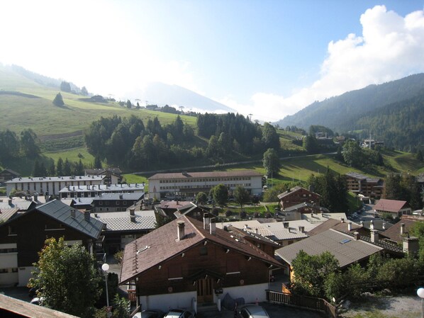 A town with traditional architecture, including a mix of residential and commercial buildings, set against a backdrop of green hills and a mountain.