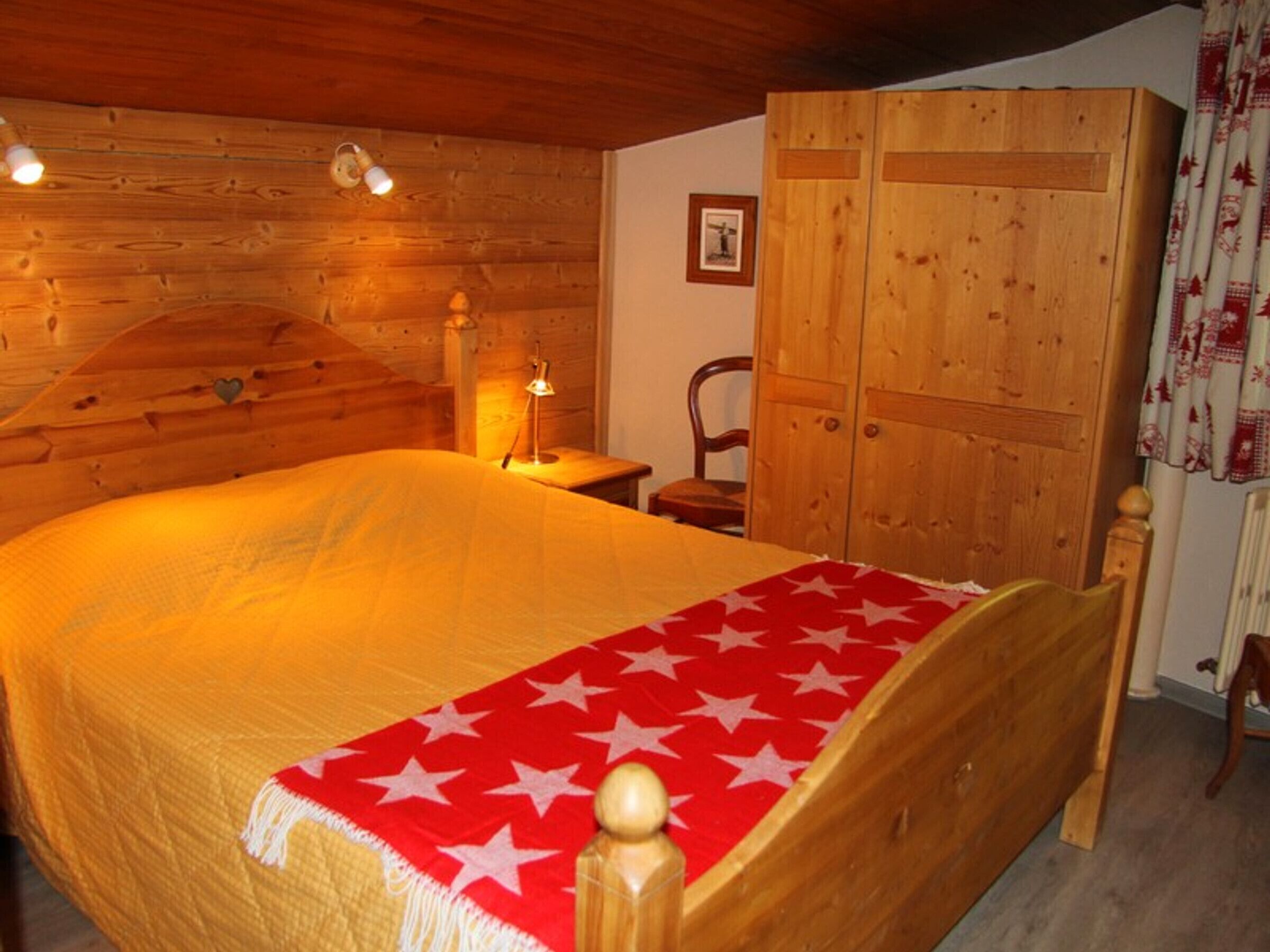 A wooden bedroom with a bed, a nightstand, a chair, and a wardrobe.