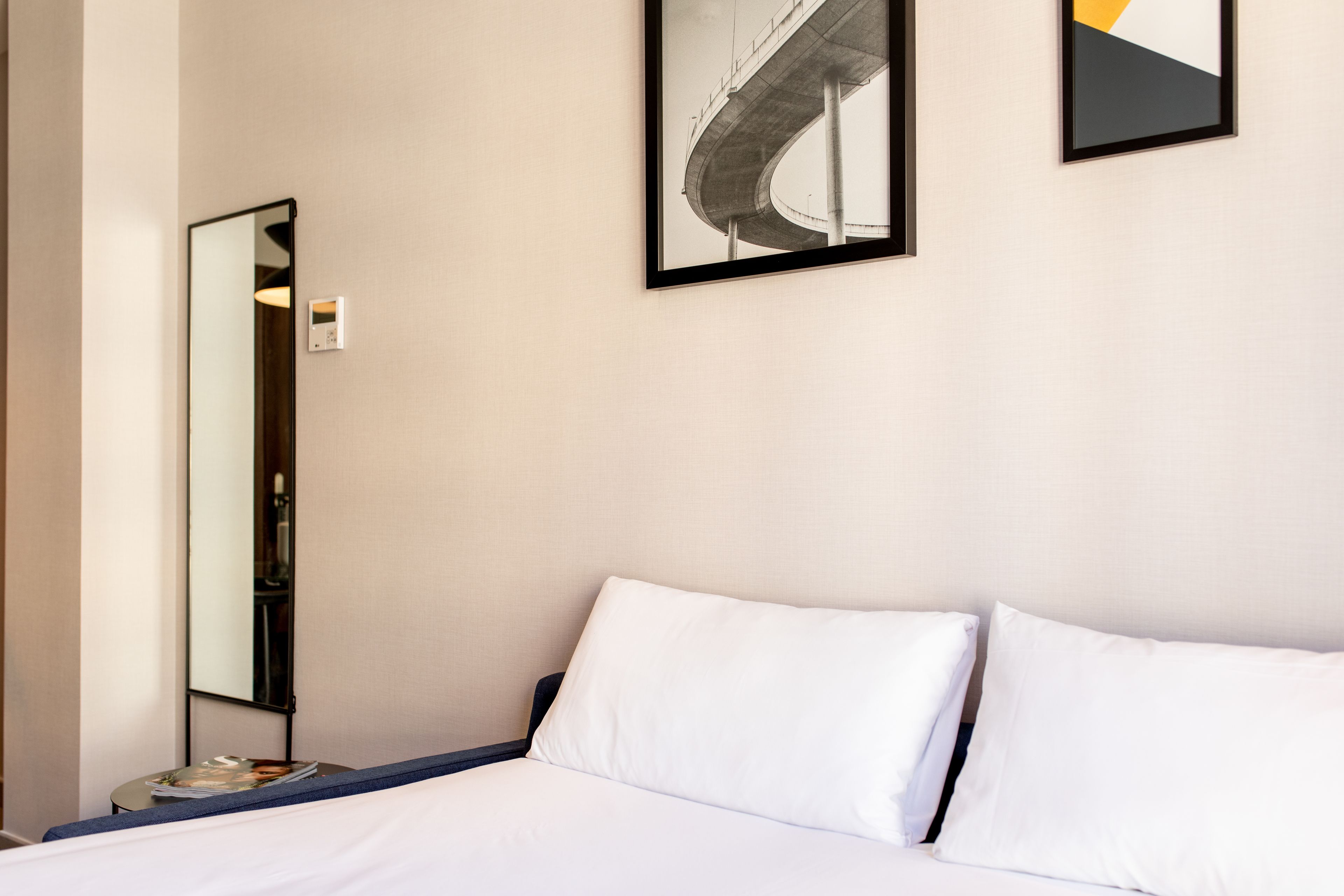 A hotel room with a bed, a nightstand, a mirror, and two framed pictures on the wall.