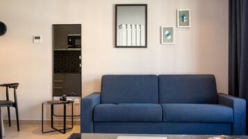 A modern living room with a blue sofa, a small table with a laptop, and a kitchen area with a microwave and cabinets.