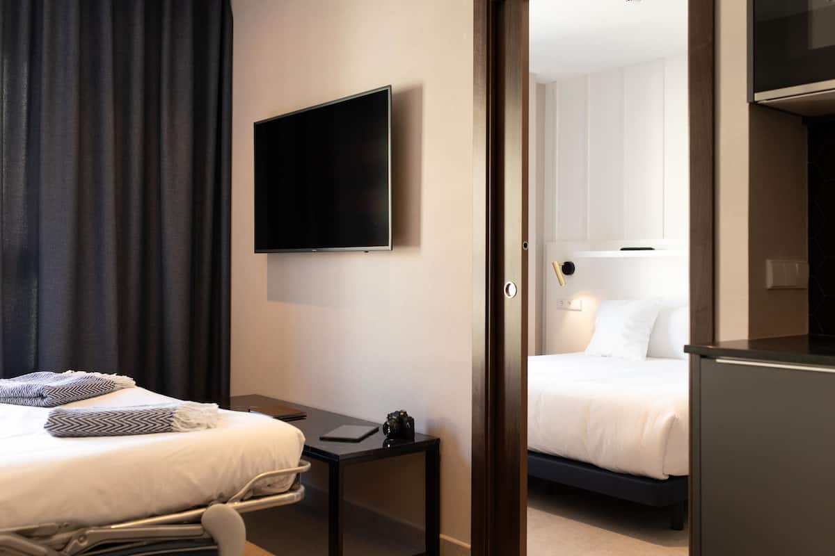 Una habitación de hotel con cama, mesita de noche y televisor montado en la pared.