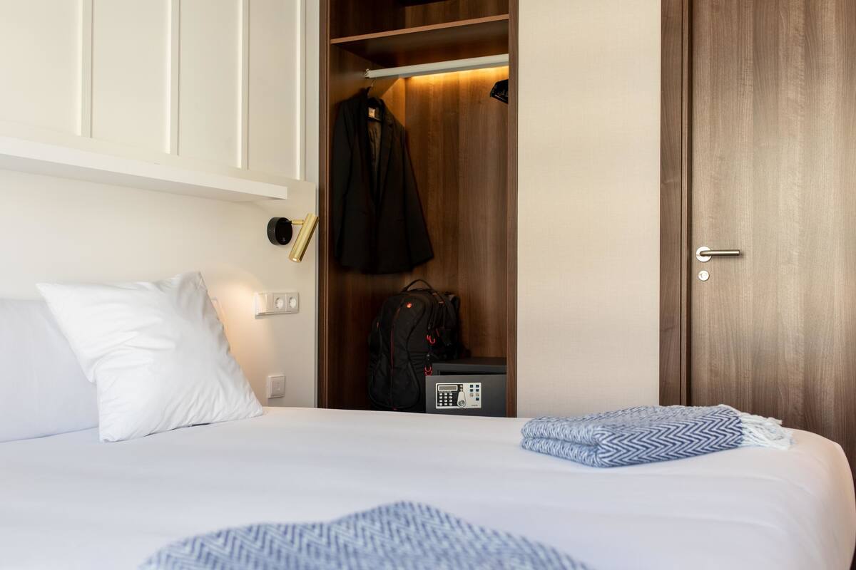 Habitación de hotel con cama, armario y escritorio con teléfono.